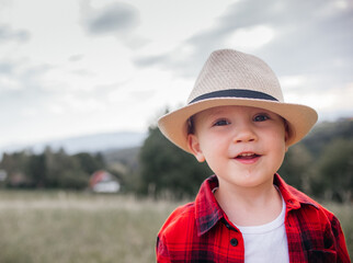 Wall Mural - boy of two years old in a hat and red shirt in a field