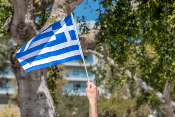 Flag of Greece in human hand on trees background.