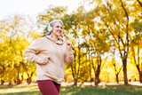Fototapeta Przestrzenne - Happy senior woman in headphones listening music while jogging outside in city park.