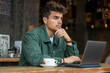© Connect Images - Man pondering at laptop in a cafe.
