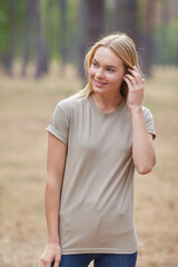 Wall Mural - Blonde lady with natural makeup posing in a pine forest. Gorgeous blue eyed caucasian woman in beige t-shirt , enjoying summer vacation.