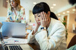 © Marko Geber - Stressed businesswoman with headache working at office desk with colleagues