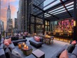 A rooftop bar with a view of the city skyline. The bar is filled with couches and chairs, and there are several tables with drinks and snacks. The atmosphere is lively and inviting