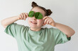 A little cheerful, smiling girl covered her eyes with spinach leaves. Concept of healthy eating, healthy children