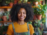 Fototapeta Uliczki - A woman with curly hair is smiling and wearing a yellow shirt and a green apron. She is holding a plant in her hand