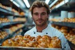 Attractive Baker in white uniform holding a tray with freshly baked bagels on the background of a bread factory or bakery.  chef holding baking tray with buns