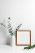 Blank square wooden frame mockup with botanical decor in white room interior, copy space