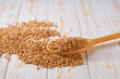 Raw organic wheat crumble from in a wooden spoon on a white wooden table.