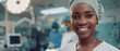 Photograph of a beautiful black female nurse, doctor, and surgeon smiling and kindly looking at the camera in a modern hospital ward with advanced medical equipment.