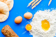 Ingredients for homemade bread. Bread near wheat ears, flour and eggs on blue background top view