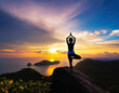 Silhouette of woman practicing yoga on the rocky hill at dawn
