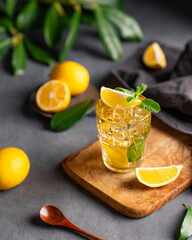 Wall Mural - A glass of iced tea with lemon and mint on a wooden board on a dark background with citrus fruits and branch.