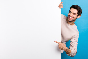 Poster - Portrait of nice young man behind empty space board point finger wear beige sweatshirt isolated on blue color background
