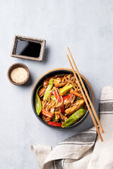 Stir-fry with soba noodles, meat and vegetables on a light background with chopsticks, soy sauce and sesame seeds.