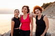 Three mid adult athletic Caucasian women in sportswear pose against background of sunset and sea. Concept of wellness and female friendship