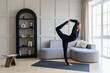 Yoga woman performing a variation of Natarajasana exercise, king of dance pose, training in black sportswear in the room standing on a mat, full length view, healthy lifestyle