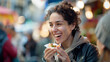 A woman sampling street food at a lively outdoor market, her expression one of pure enjoyment. Shallow depth of field, blurred background