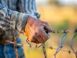 Close-up of a farmer tightening a fence wire, with a blurred pasture behind