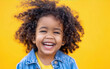 Portrait of a joyful kid with curly hair wearing a blue jean jacket against a yellow background