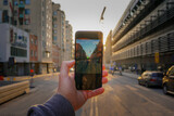 Fototapeta Boho - Cropped hand holding a mobile phone against city street