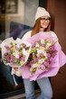 Colorful flowers in the hands of a cheerful girl who stands in a sweater and jeans