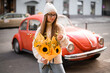 Retro car and a young girl in glasses and sweater stands with a bouquet
