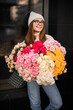 Perky girl in light sweater and jeans stands with a bouquet of colorful flowers