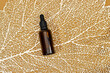 Blank amber glass essential oil bottle on podium stand on golden line leaf texture. Skin care concept with natural cosmetics
