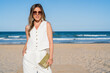 Elegant woman with sunglasses and white dress posing on the beach on a sunny day