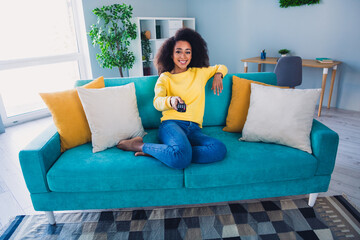 Wall Mural - Photo of adorable cheerful girl sitting on couch turning on tv watching movie in cozy apartment daylight indoors