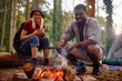 Happy multiracial couple enjoying by bonfire while camping in nature.