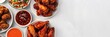 A white background with a variety of chicken wings and dipping sauces. Concept of abundance and indulgence, as there are many different types of wings and sauces to choose from