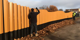 Fototapeta Przestrzenne - A man diligently works on a wooden fence, his hands busy crafting each plank with care and precision.