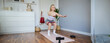 Portrait of young woman, fitness instructor making a video for sport vlog, doing squats on camera, using resistance band, working out at home
