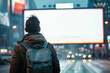 A man wearing a backpack is standing in front of a large billboard. The billboard is empty, and the man is looking at it. The scene takes place in a city, with cars