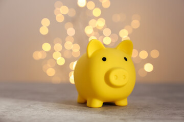 Poster - Yellow piggy bank on grey table against blurred lights, space for text