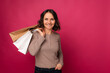 Studio portrait of a smiling mid age woman holding some shopping bags o ver pink background.