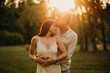 Young handsome man kisses gentle his wife on forehead while embracing her at sunset in park.