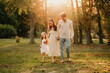 Wonderful young laughing family of three are walking barefoot on grass at sunset.
