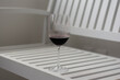 A glass with some red wine on top of a white wooden chair.