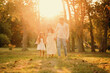Wonderful young family of three are walking barefoot on grass while holding hands at sunset.