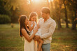 Young mother and father are holding up in arms their cute daughter in park at sunset.