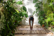 Concentrated african american woman standing on fitness mat among green houseplants at home garden. Pleased black woman stretching, practice yoga with awareness to physical body health in urban jungle