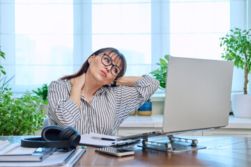 Wall Mural - Tired middle-aged woman sitting at her workplace, desk with computer