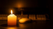 A white burning candle in close-up on a desk against a computer out of focus in black background