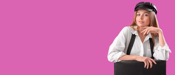 Stylish young woman with suspenders sitting in chair on purple background