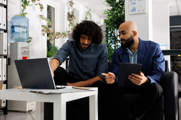 Wall Mural - Entrepreneur and colleague discussing project while analyzing data on laptop in business office. Arab employees planning product promotion strategy together in coworking space