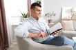 © Pixel-Shot - Young man reading book in armchair at home