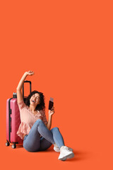 Poster - Cheerful African-American female tourist with suitcase and passport on orange background