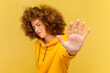 Portrait of scared woman with Afro hairstyle making stop gesture showing palm of hand, conflict prohibition warning about danger, stop bullying. Indoor studio shot isolated on yellow background.